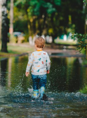 Su birikintisinde lastik botla yürüyen mutlu çocuk. Geri görünüm
