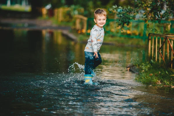 Niño feliz jugando en charco con botas de goma. Un chico se divierte después de una lluvia . —  Fotos de Stock
