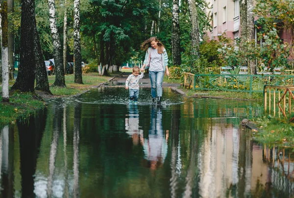 Happy mother and son stroling in big puddle after a rain thunderstorm on a bright summer day outside. — Stock Photo, Image