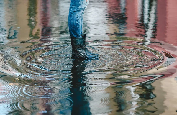 雨后,妇女们穿着黑色橡胶靴和蓝色牛仔裤,站在水坑里。侧视图 — 图库照片