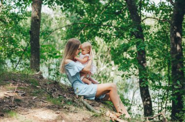 Uzun saçlı güzel anne çimenlerin üzerinde oturan ve yaz ormanında küçük bir kızı ile oynarken
