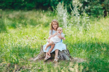 Arka planda yeşil çayır ile kütükler üzerinde oturan iki sevimli genç kız kardeş