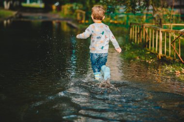 Bir yağmurdan sonra su birikintisi üzerinde yürüyen sevimli çocuk 