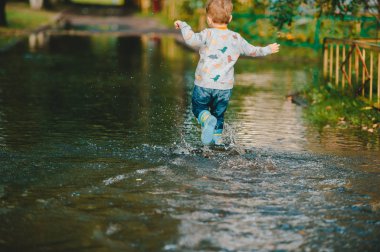 Yağmurdan sonra çocuk. Sevimli mutlu çocuk çocuk su birikintisi oynuyor. Geri görünüm