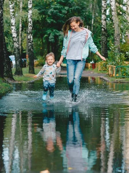 Niño con su madre caminando sobre los charcos después de la lluvia. Vista vertical . —  Fotos de Stock
