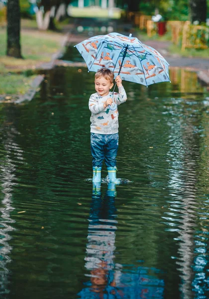 Criança com um guarda-chuva colorido em uma poça após a chuva . — Fotografia de Stock