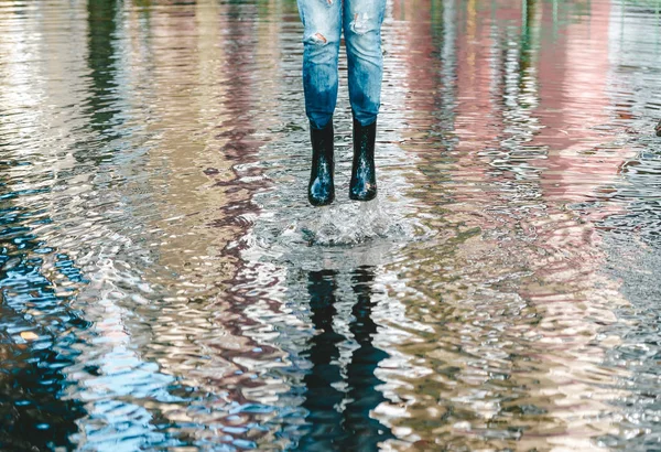 Flicka med svarta stövlar hoppar i pöl efter ett regn i sommardag. Regnväder koncept. — Stockfoto