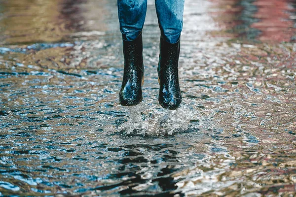 Legs of woman in shabby jeans and in rubber boots jump in big puddle