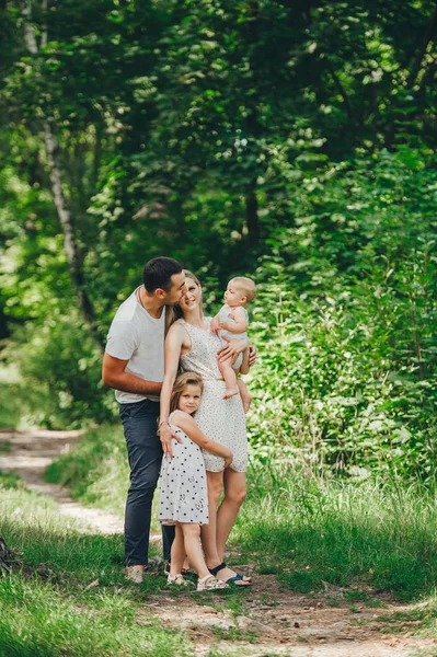 Happy young family spending time together in green nature park. Mother and father kissing baby daughters. — Stock Photo, Image