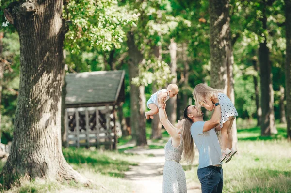 Mom, dad and little daughters playing in the summer park near big trees. — Stock Photo, Image