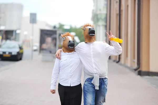 Casal usando máscaras de cavalo andando na rua da cidade . — Fotografia de Stock