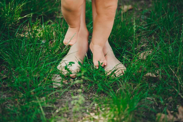 Legs of mother and her baby walk on green grass barefoot in garden. — Zdjęcie stockowe