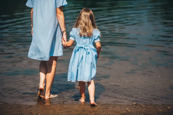 Young woman and her daughter barefoot walk in the water on a river. Back view. Closeup — Stock Photo, Image