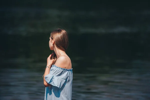Piękna zmysłowa kobieta z długimi włosami w niebieskiej sukni pozowanie na brzegu jeziora w letni dzień — Zdjęcie stockowe