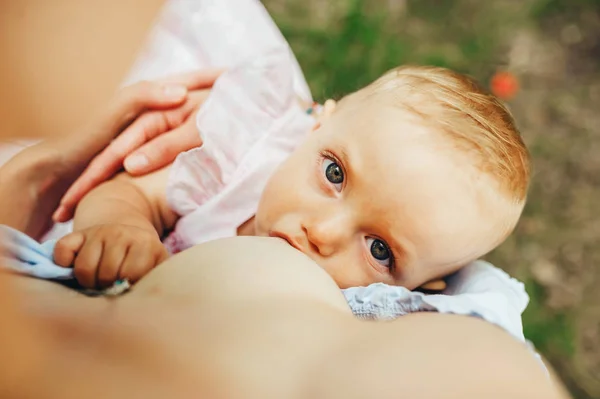 Young mom breastfeeding newborn outside. Baby child is looking to camera. — Stock Photo, Image