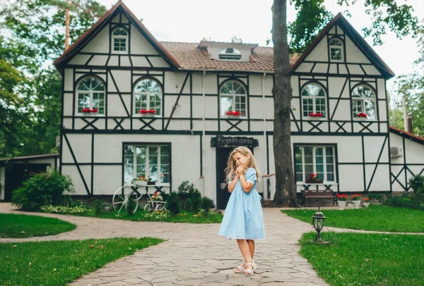 Entzückendes kleines Mädchen in blauem Kleid steht in der Nähe von Hotel. — Stockfoto