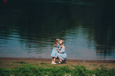 Anne kucaklar ve gün batımında yaz aylarında göl kıyısında oturan küçük kızı öpmek.