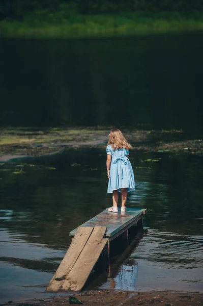 孤独的小女孩站在木码头上。后视图 — 图库照片