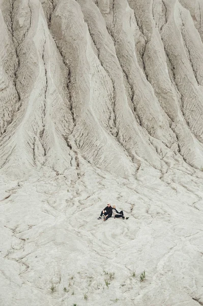 Para turystyczna siedzi razem w oddali na białym piasku geologicznej i przemysłowej dzielnicy w Rummu. Estonia. — Zdjęcie stockowe