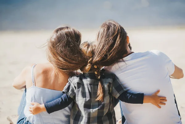 Vista trasera de la familia feliz disfrutando del fin de semana, sentado en la arena en una playa —  Fotos de Stock