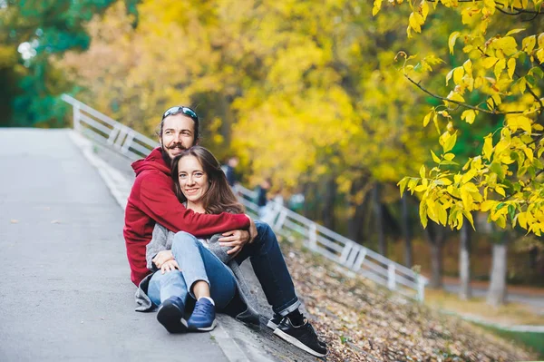 Hermosa pareja joven feliz sentarse y se abraza en el borde de la carretera en la temporada de otoño . —  Fotos de Stock