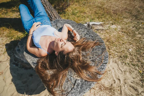 性感的女孩模型在蓝色牛仔裤睡在户外的木桩上。顶部视图 — 图库照片