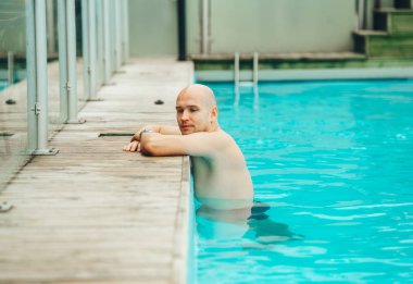 Ciddi kel adam yüzme havuzunda dinlenme ve gülümseyen rahatlatıcı