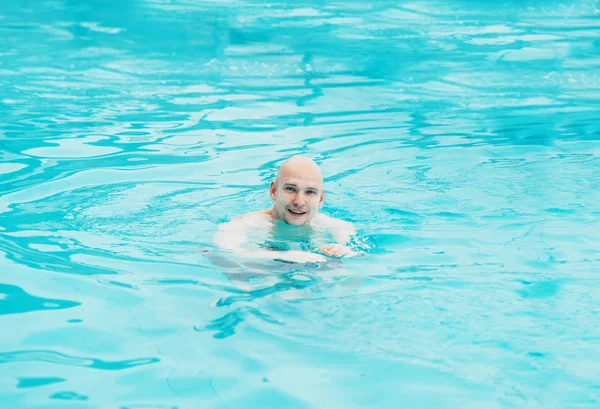 Bonito homem careca relaxante descansando na piscina e sorrindo — Fotografia de Stock