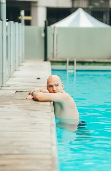 Σοβαρός φαλακρός άνθρωπος χαλαρωτικό αναπαύσεως στην πισίνα και κοιτάζοντας στην άκρη. Πλευρική όψη — Φωτογραφία Αρχείου