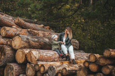 Genç anne, kızıyla sonbahar ormanlarında tahta odunlarda oynuyor.