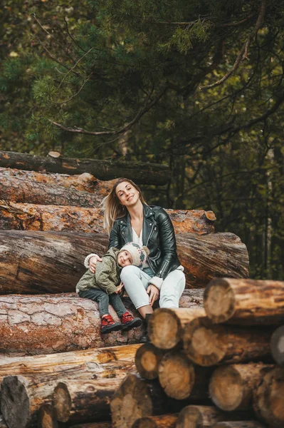 Retrato de otoño de la madre y la niña en el bosque de otoño en la pila de troncos . — Foto de Stock