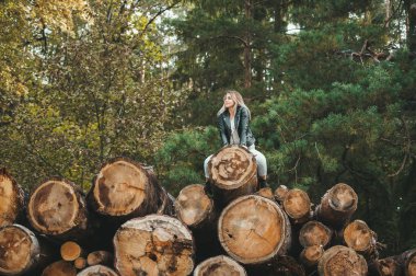 Güzel bir kadın sonbahar ormanında büyük kütüklerin üzerinde oturuyor.