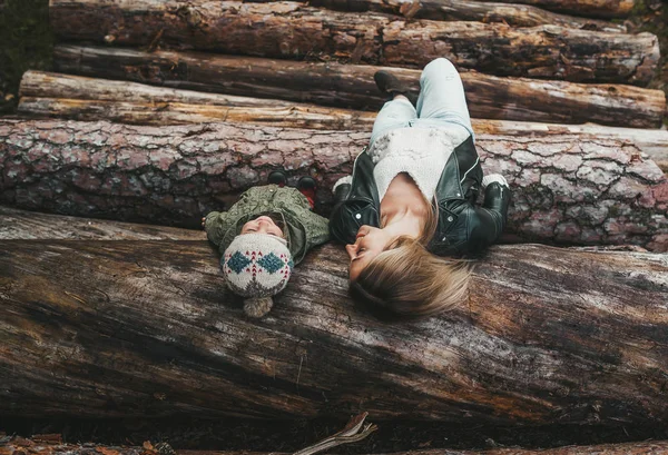 Retrato otoñal de la madre y la niña acostadas en una pila de troncos . — Foto de Stock