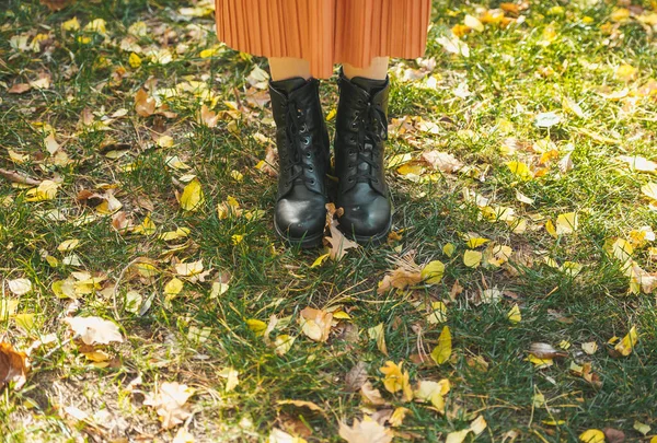 Kobiece nogi w czarnych butach na zielonej trawie pełnej kolorowych żółtych, pomarańczowych i jesiennych liści. — Zdjęcie stockowe