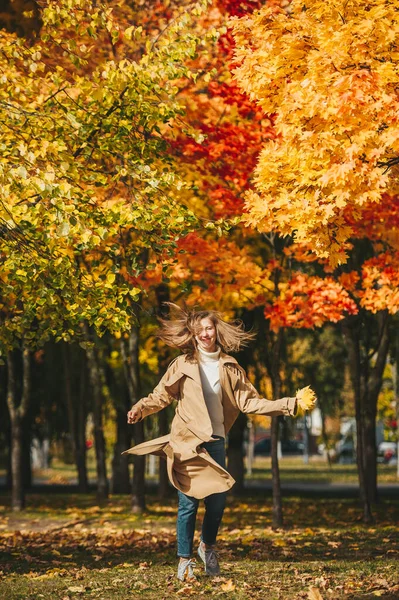 Piękna dziewczyna w płaszczu baege skoki w jesiennym parku. — Zdjęcie stockowe