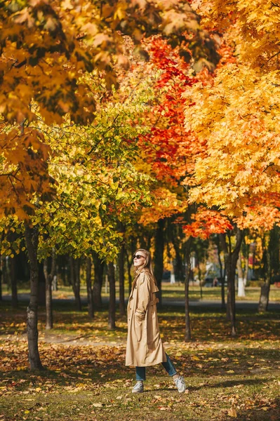 Modna szczęśliwa kobieta w płaszczu i czarnych okularach tańczy w jesiennym parku. — Zdjęcie stockowe