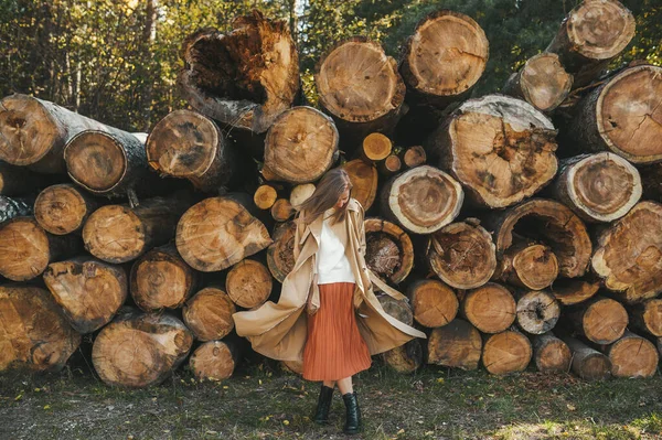 Mujer joven en abrigo beige bailando en el fondo de troncos de madera en la naturaleza. Concepto de caída — Foto de Stock