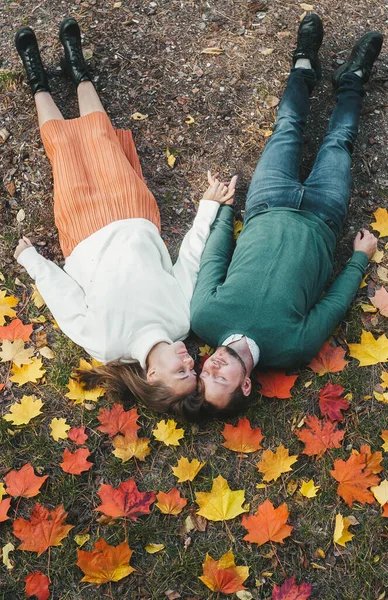 Ovanifrån unga glada glada lyckliga par i kärlek liggande på fallna löv i höstens stadspark utomhus. — Stockfoto