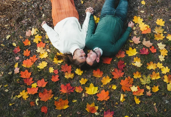Glada unga par tittar på varandra medan de ligger på marken med gula blad på. Ovanifrån. — Stockfoto