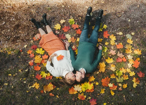 Ovanifrån unga glada glada lyckliga par i kärlek liggande på fallna löv i höstens stadspark utomhus. — Stockfoto