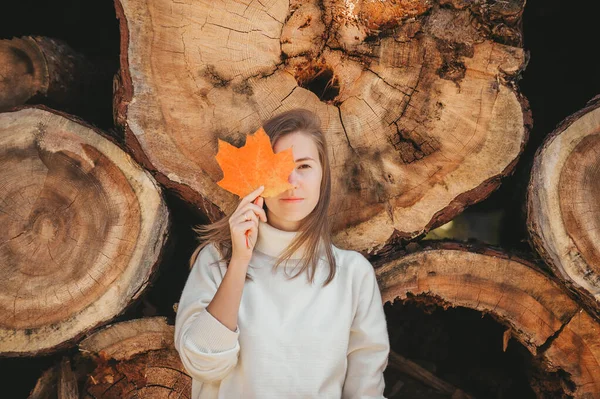 En otoño mujer día escondido detrás de la hoja de arce colorido, hermoso en el fondo de leña y troncos . — Foto de Stock