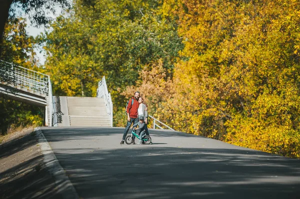 Η μητέρα, ο πατέρας και ο μικρός γιος στο ποδήλατο ποζάρουν στο πάρκο το φθινόπωρο στο βάθος της ηλιόλουστης ημέρας — Φωτογραφία Αρχείου