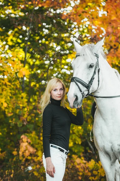 Söt ung kvinna med en vit häst ridning i höst dag — Stockfoto