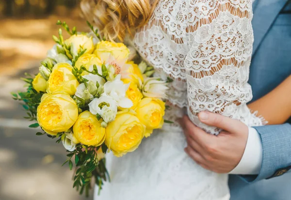 Mãos de noivo com um buquê de casamento abraçando as costas da noiva . — Fotografia de Stock