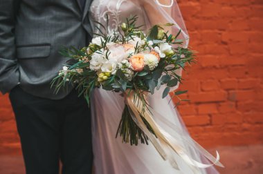 Gelinlik buketli düğün çifti kırmızı tuğla duvarın yanında duruyor.