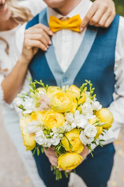 Sposa corregge il papillon allo sposo. Bouquet da sposa con rose gialle . — Foto Stock