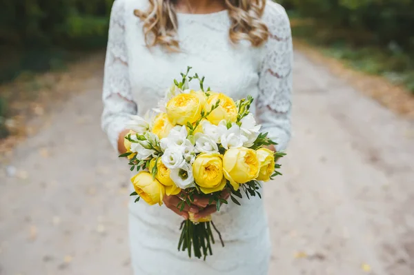 Una donna caucasica è in piedi sul sentiero, in possesso di un bouquet da sposa di rose gialle con indosso un abito da sposa . — Foto Stock