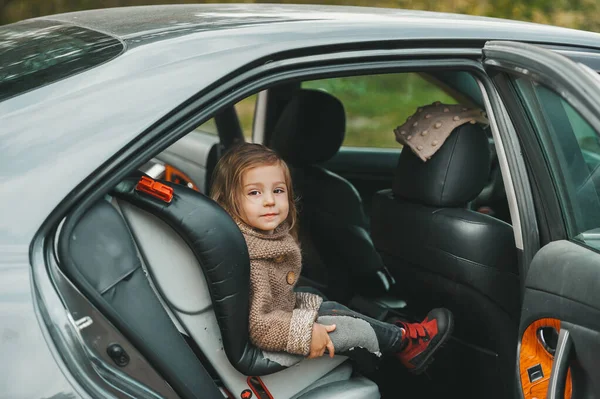 Little girl in sweater sitting in the car in child safety seat and smiling — Stock Photo, Image
