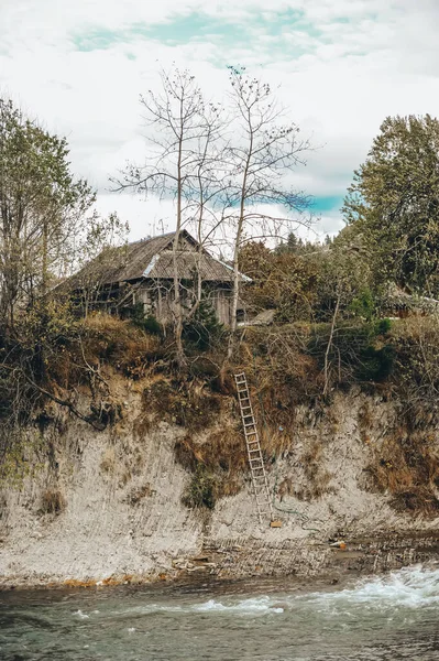 Antigua cabaña de madera y raíces abiertas de árboles en la empinada orilla del río . — Foto de Stock