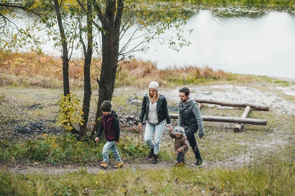 Mama, tata i małe dzieci, spacerujące po jesiennym lesie w pobliżu rzeki. Rozmawiają i cieszą się pięknym jesiennym dniem.. — Zdjęcie stockowe